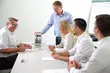 Group of professionals examining a blue industrial pump on a table, discussing its components and functions.
